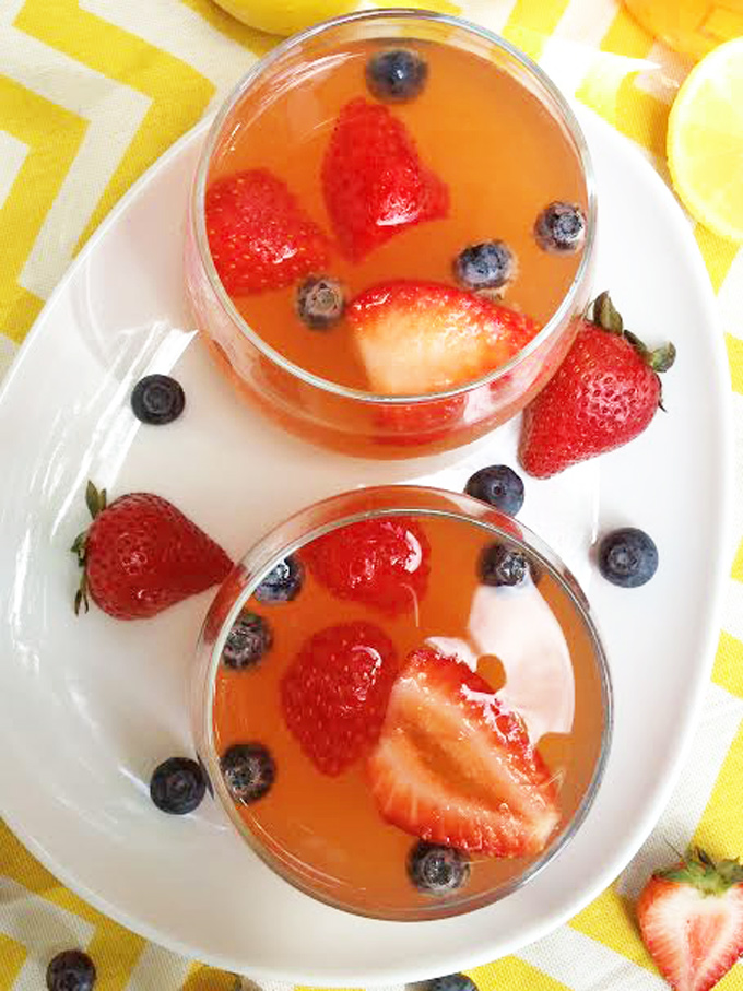 Overhead shot of two glasses filled with Strawberry Infused lemonade garnished with sliced strawberries and blueberries on a white platter.