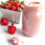 Jar of strawberry coconut butter with a white berry basket filled with fresh strawberries and two fresh strawberries on the table next to the jar.