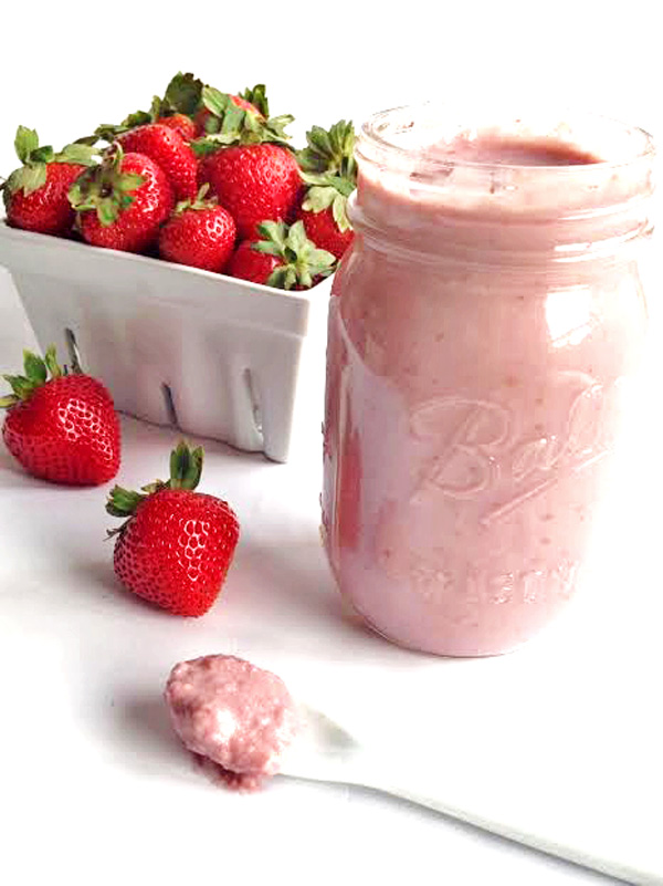 Jar of strawberry coconut butter with a white berry basket filled with fresh strawberries and two fresh strawberries on the table next to the jar.