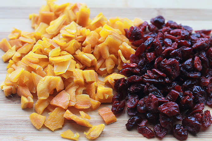 Chopped dried mango and dried cranberries on a bamboo cutting board.