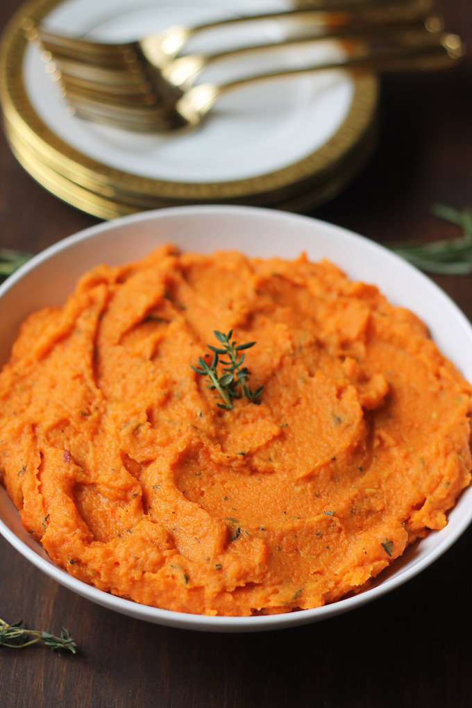 Rosemary and thyme creamy carrots on a bowl with a stack of plates with forks on the plates behind the bowl of creamy carrots.