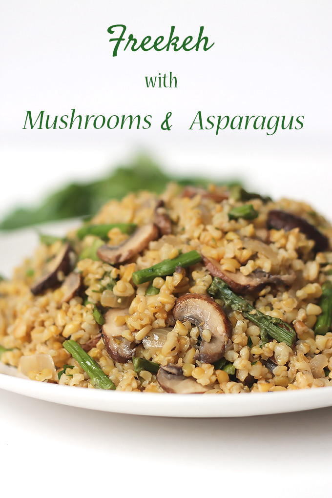 White plate filled with Freekeh with mushrooms and asparagus with green herbs in the background.