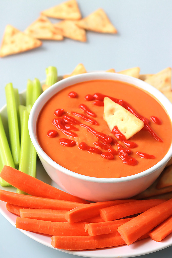 Full-Bowl-of-Red-Lentil-&-Roasted-Red-Pepper-Sauce With carrot and celery sticks on a white plate.