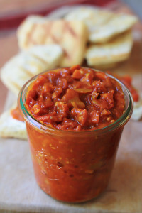 Roasted tomato chutney in a weck jar with slices of crusty bread in background.