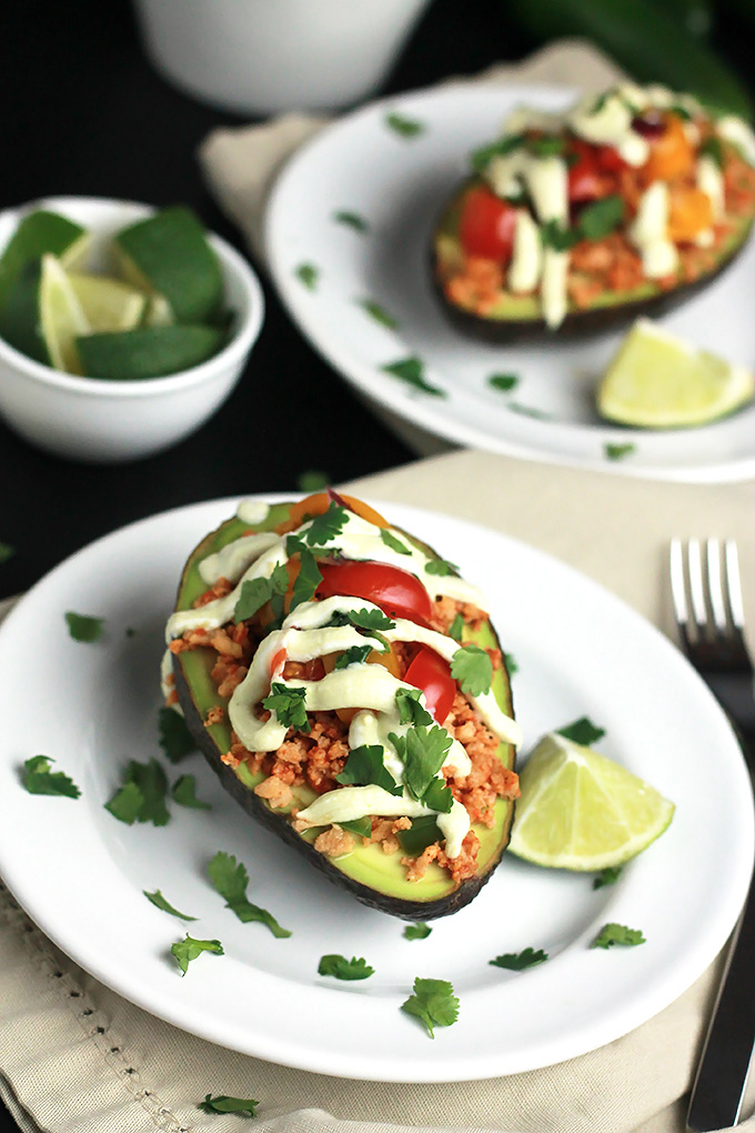 Sliced avocado stuffed with textured vegetable protein, topped with avocado cream, tomatoes and cilantro, with a wedge of lime.