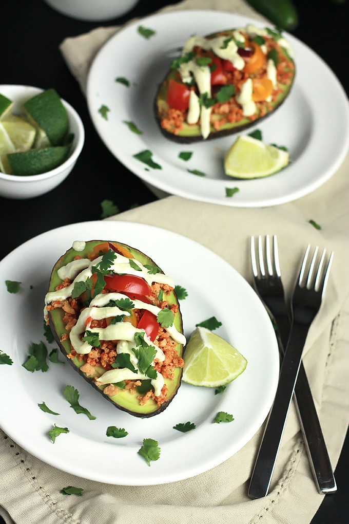 Sliced avocado stuffed with textured vegetable protein, topped with avocado cream, tomatoes and cilantro, with a wedge of lime.
