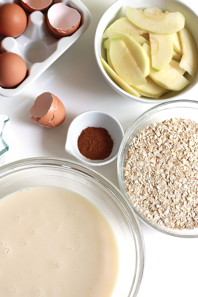 Above cracked eggs shells, bowl of sliced apples, bowl of oats and bowl of almond milk.