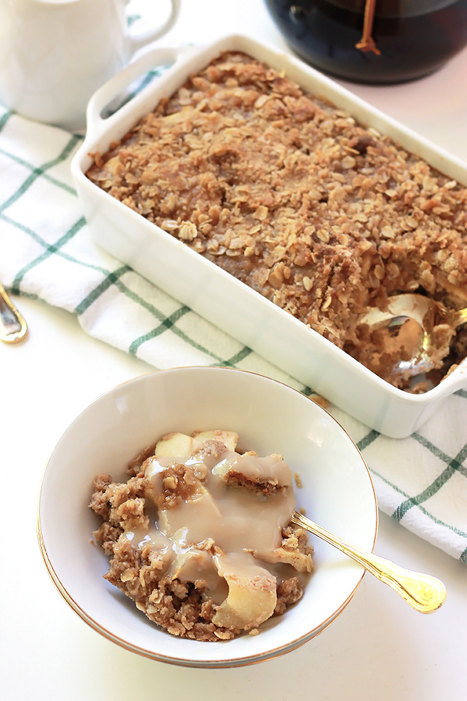 Bowl of Apple Cinnamon Baked Oatmeal topped with brown sugar sauce. Remaining Apple Cinnamon Baked Oatmeal in white baking dish beside bowl.