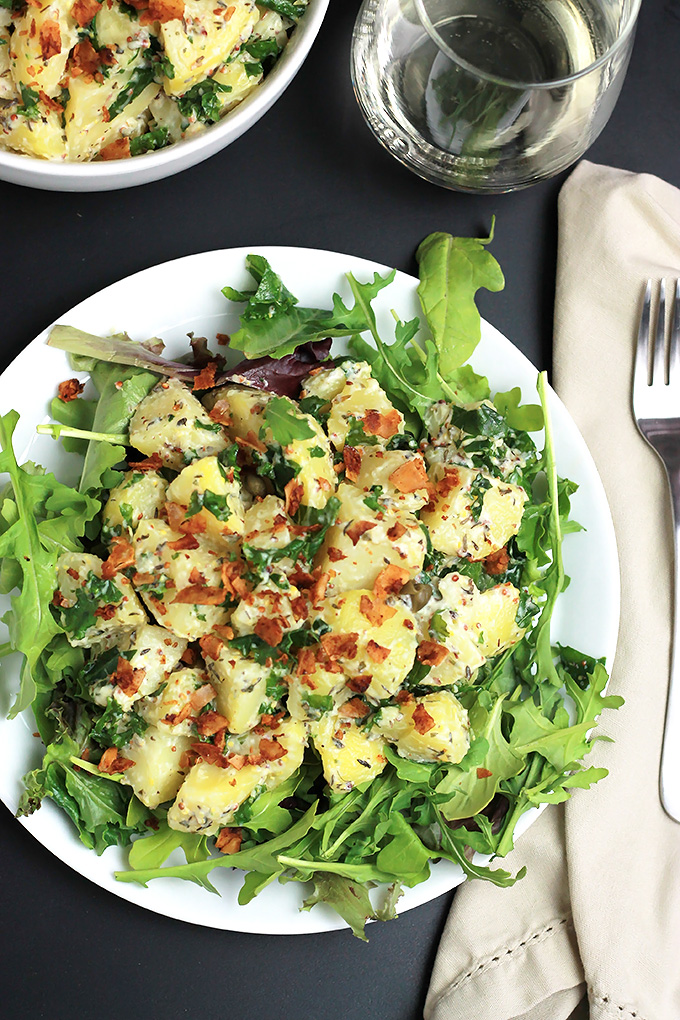 Overhead shot of Vegan Yukon Kale Potato Salad on a bed of arugula with coconut bacon on top.