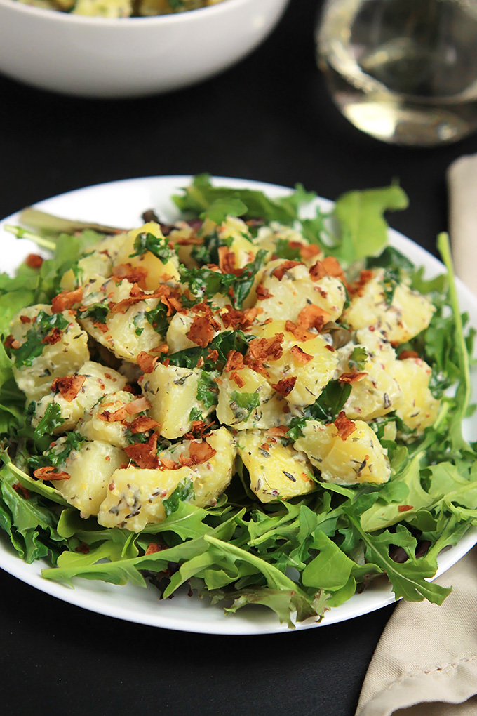 Vegan Yukon Kale Potato Salad on a bed of arugula with coconut bacon on top.