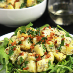 Vegan Yukon Kale Potato salad on white plate with vegan coconut bacon on top.