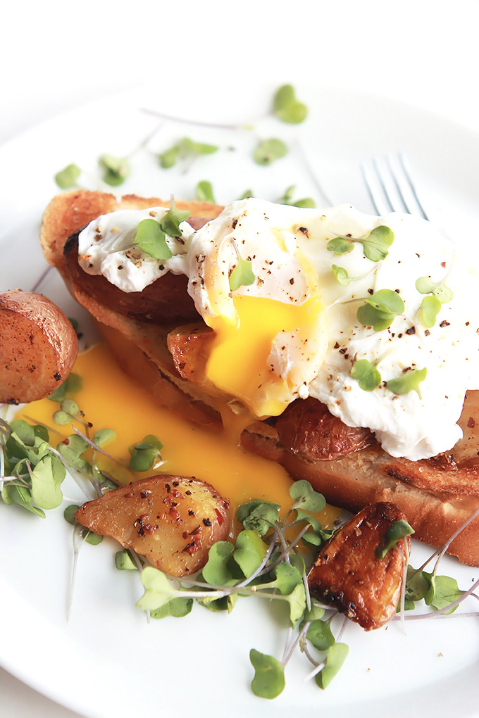 Poached egg over toast and roasted potatoes, garnished with greens.