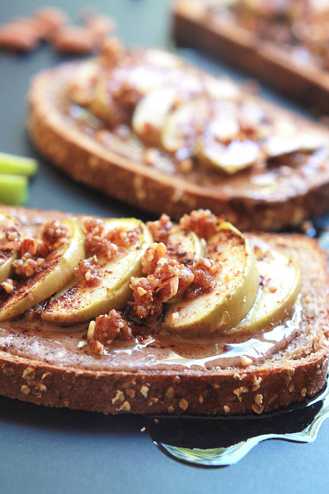 Close-up of whole wheat toast layered with almond butter, sliced apples, sprinkled with almond and date mixture.