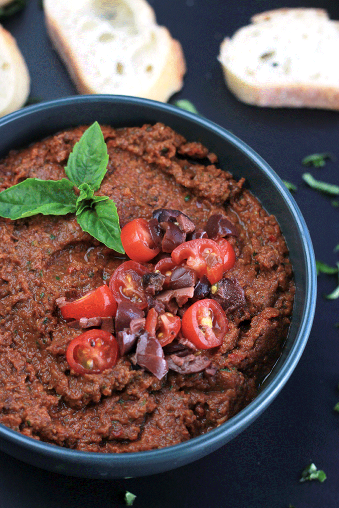 Overhead shot of Sun-Dried Tomato Tapenade garnished with sliced tomatoes and fresh basil sprig.