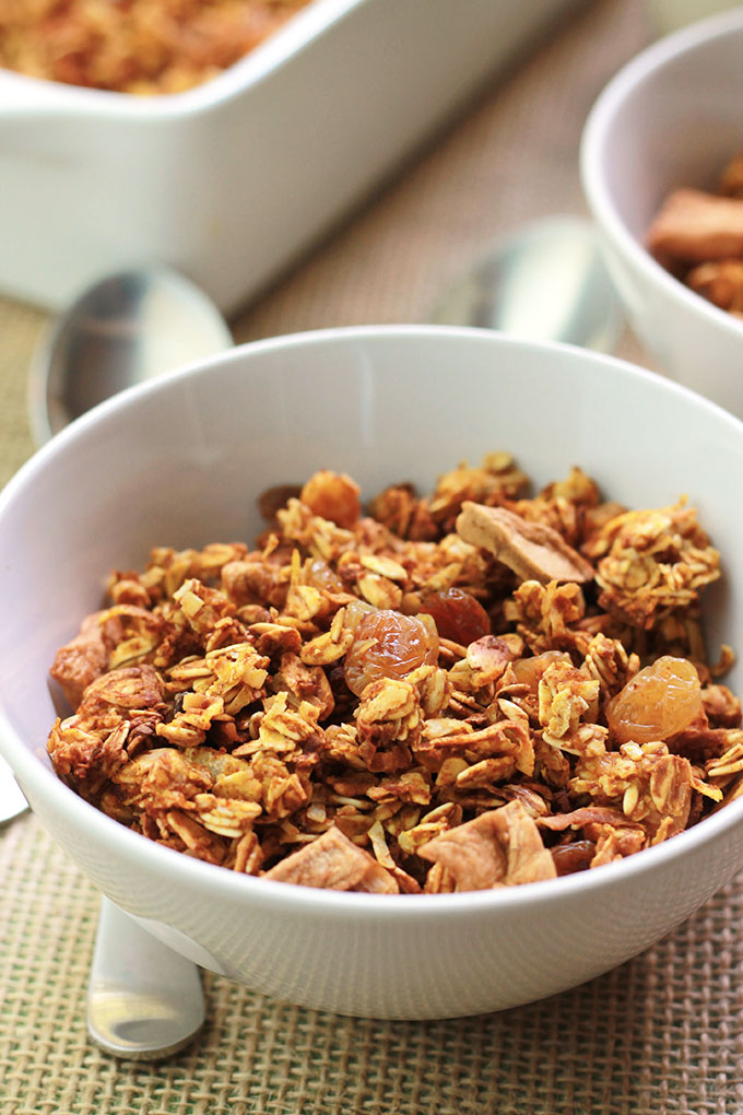 Pumpkin Apple Cinnamon Granola in a white bowl with spoon beside bowl.