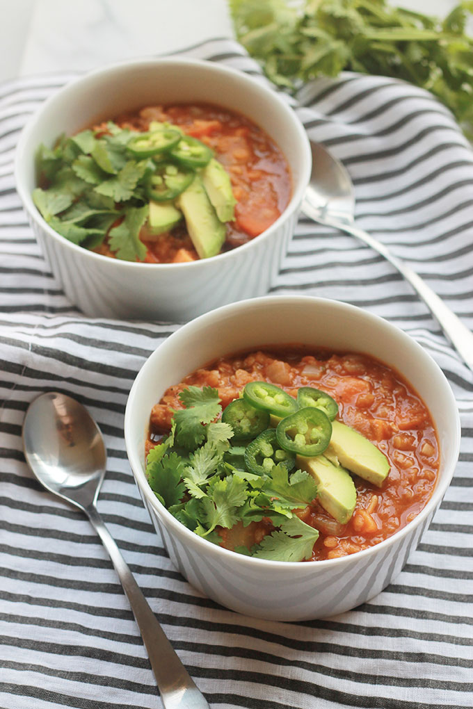 Two bowls of spicy lentil sweet potato stew with sliced avocado, jalapeno and torn cilantro leaves on top.
