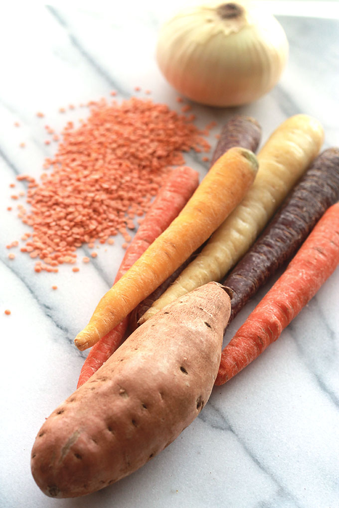 Raw onion, red lentils, rainbow carrots and sweet potato on marble counter.