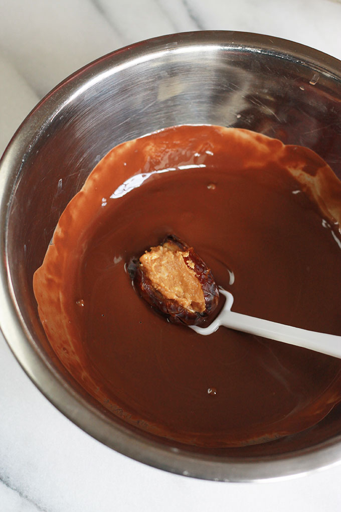 Dipping stuffed date into melted chocolate in a stainless steel bowl.