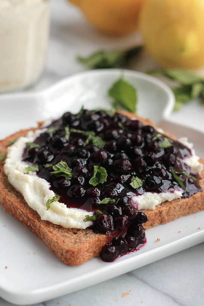 Lightly sweetened creamy lemon ricotta on toast topped with sweet juicy wild blueberry compote, sprinkled with mint. Sumptuosity on a plate.
