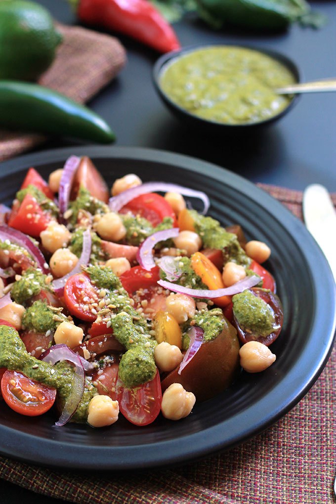 Cilantro Chutney with Heirloom tomato salad on a black plate.