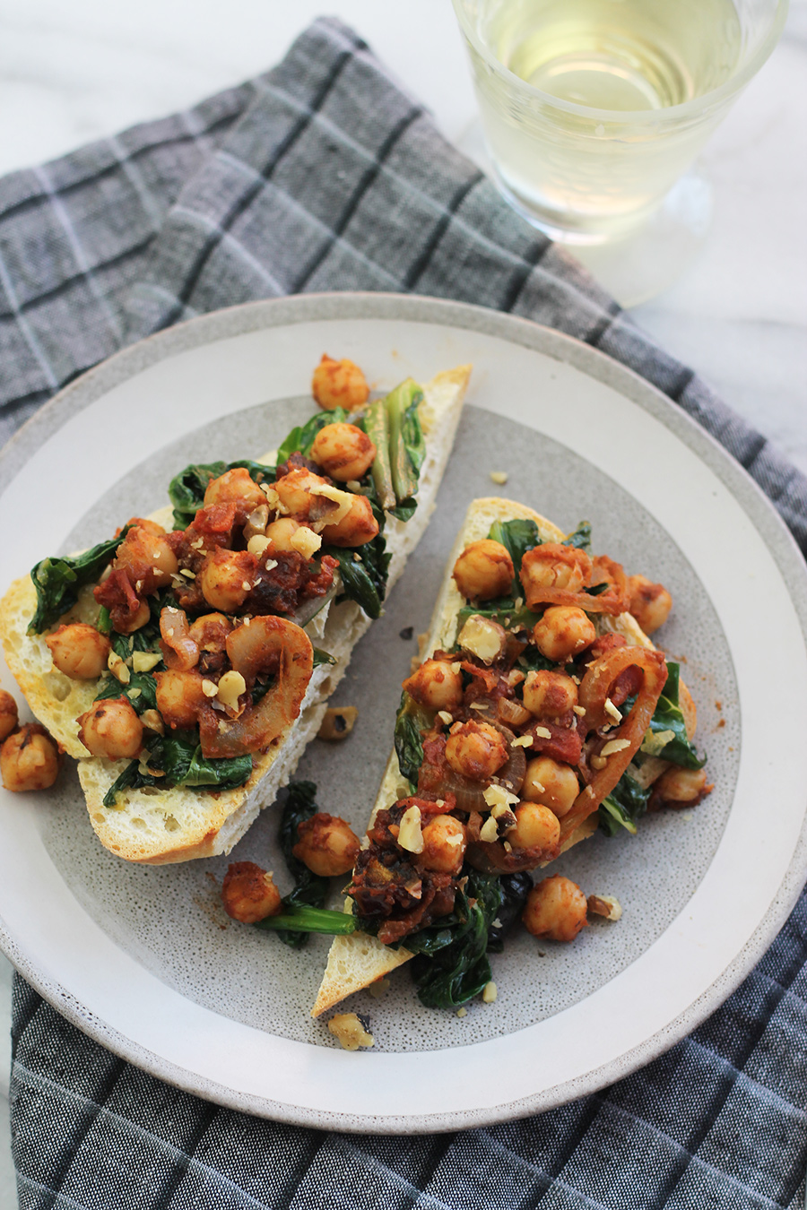 close-up shot of ciabatta garlic toast with spinach, chard and chickpeas on top, with a glass of wine in background.