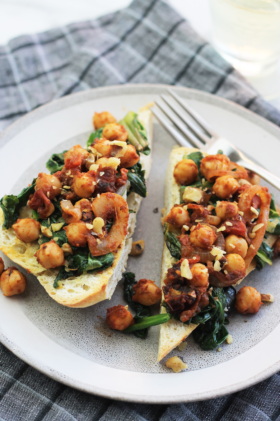 Ciabatta garlic toast with sauteed greens and chickpeas on top with a glass of wine in the background.