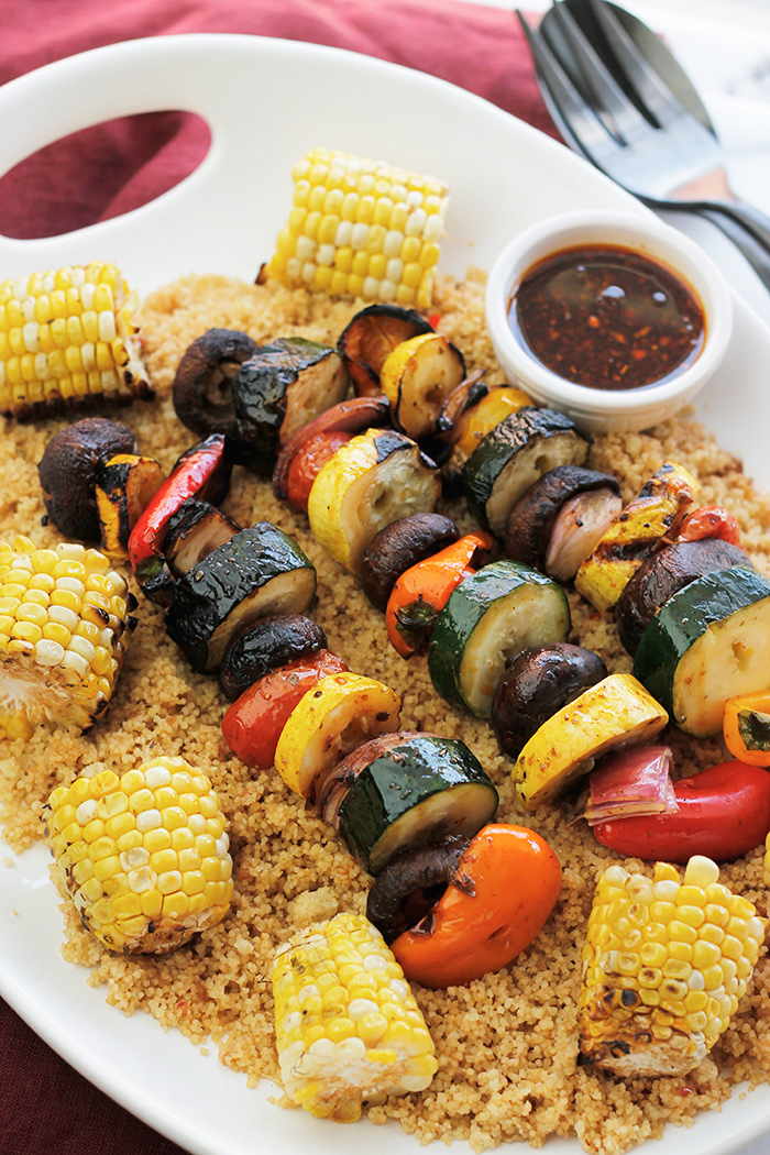 Overhead shot of grilled veggie kabobs, corn over couscous.