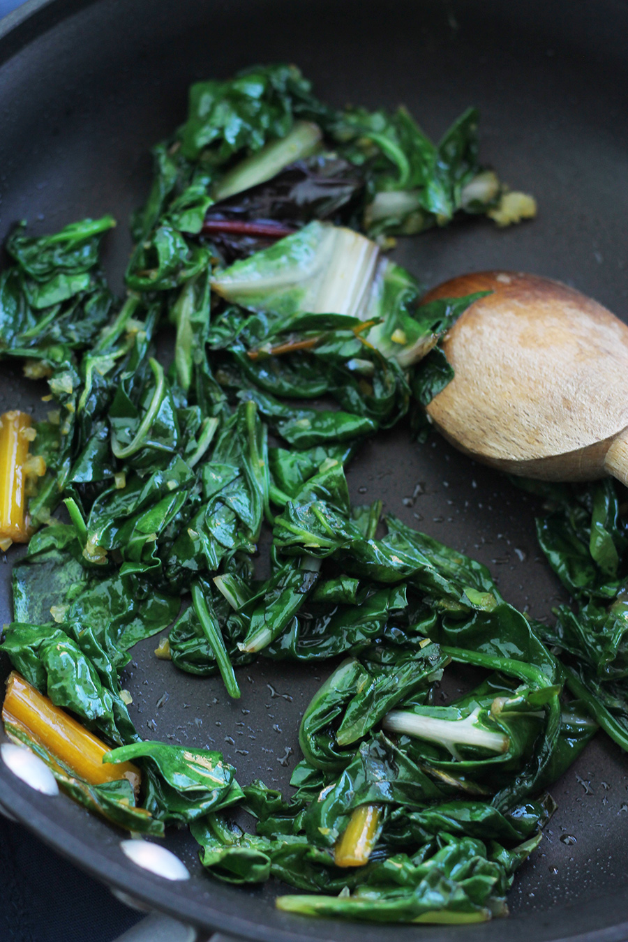 Spinach and chard in saute pan with wooden spoon on the side.