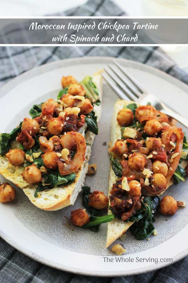 Ciabatta garlic toast with sauteed greens and chickpeas on top with a glass of wine in the background.