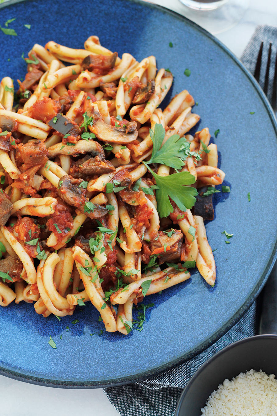 Blue plate filled with Vegan Eggplant Mushroom Bolognese Sauce tossed with Casarecce pasta.