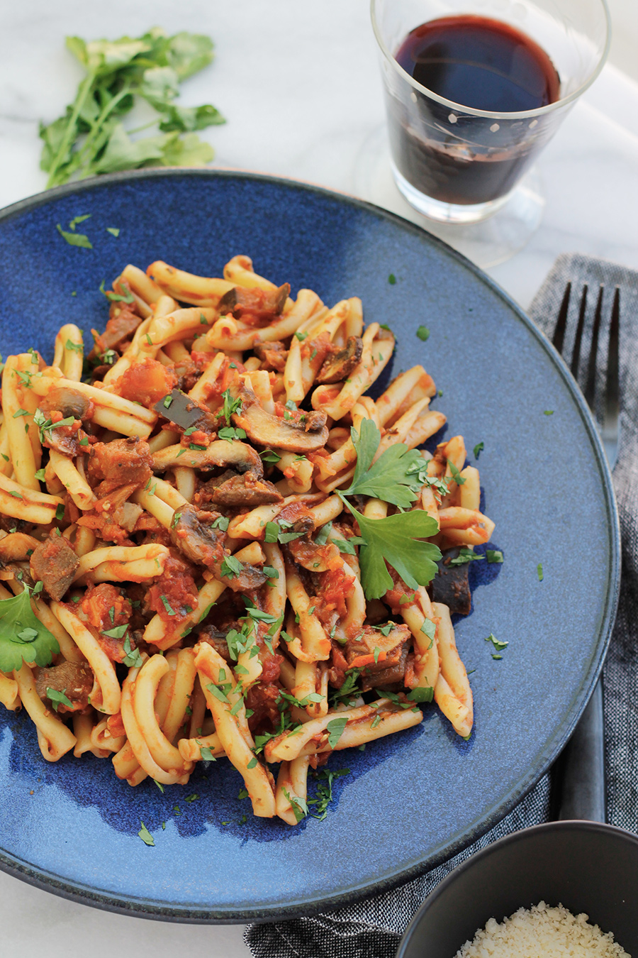 Overhead shot of Vegan Eggplant Mushroom Bolognese tossed with Casarecce on a blue plate with a glass of red wine.