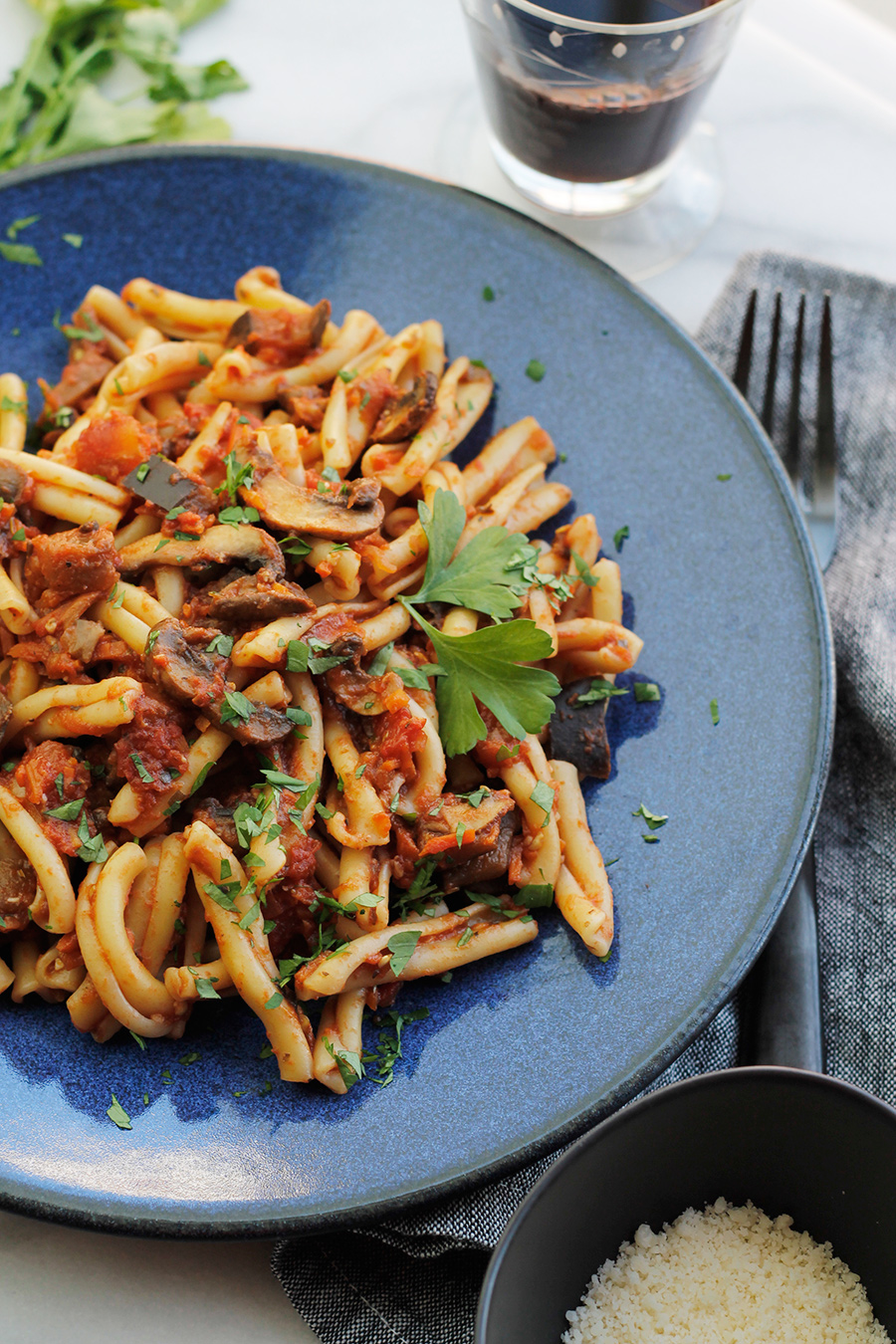 Overhead shot of Vegan Eggplant Mushroom Bolognese tossed with Casarecce on a blue plate with a glass of red wine.