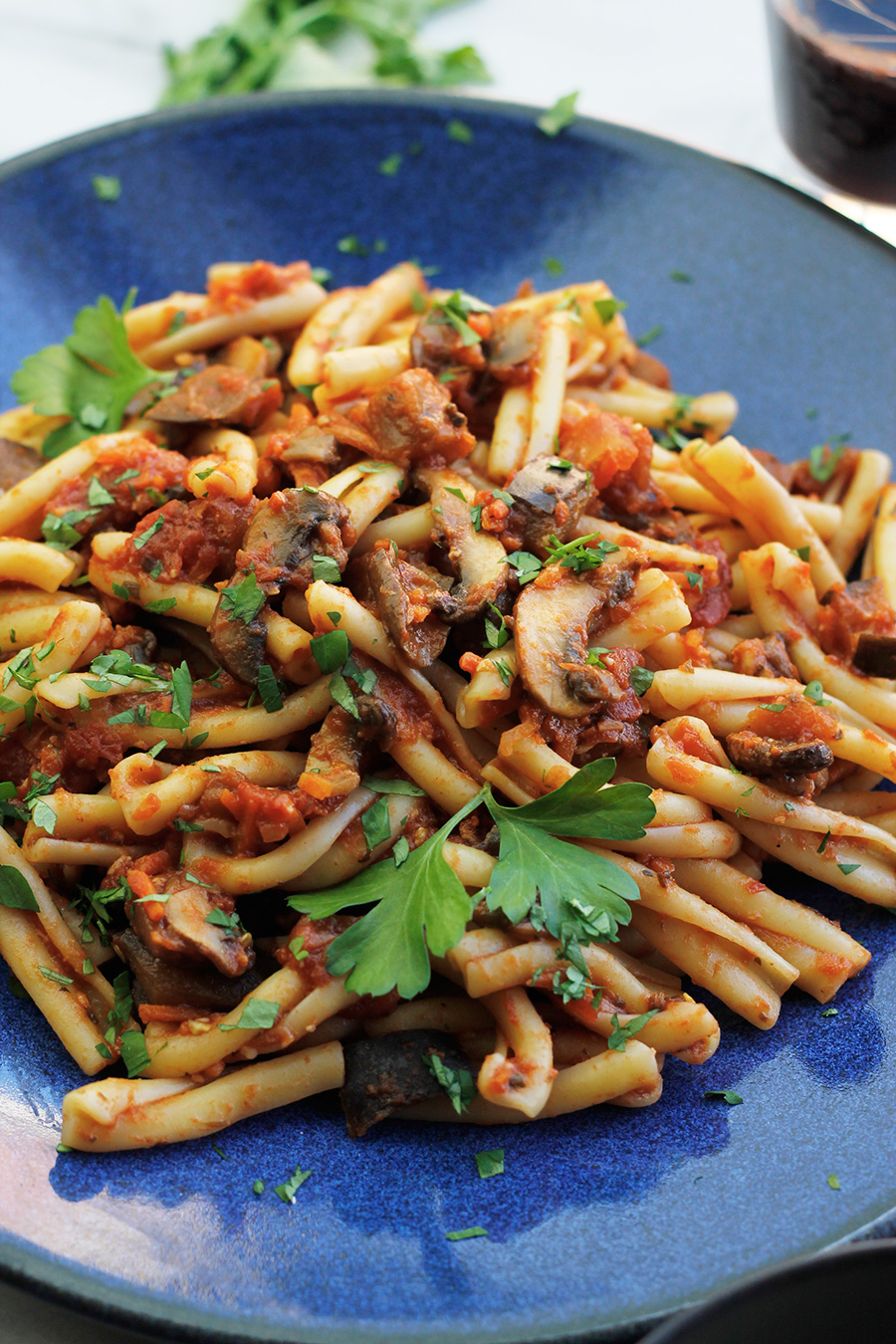 Close-up of blue plate filled with Vegan Eggplant Mushroom Bolognese Sauce tossed with Casarecce pasta.
