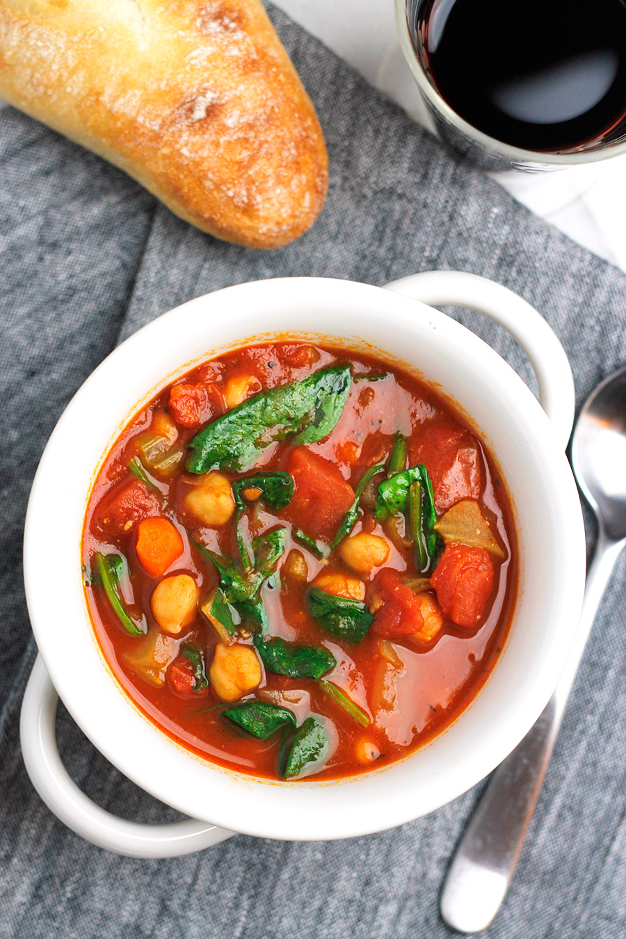 Overhead shot of Sun-Dried Tomato and Chickpea Soup with crusty bread and glass of red wine.