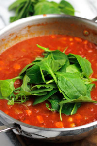 Pot of soup with spinach and arugula on top.