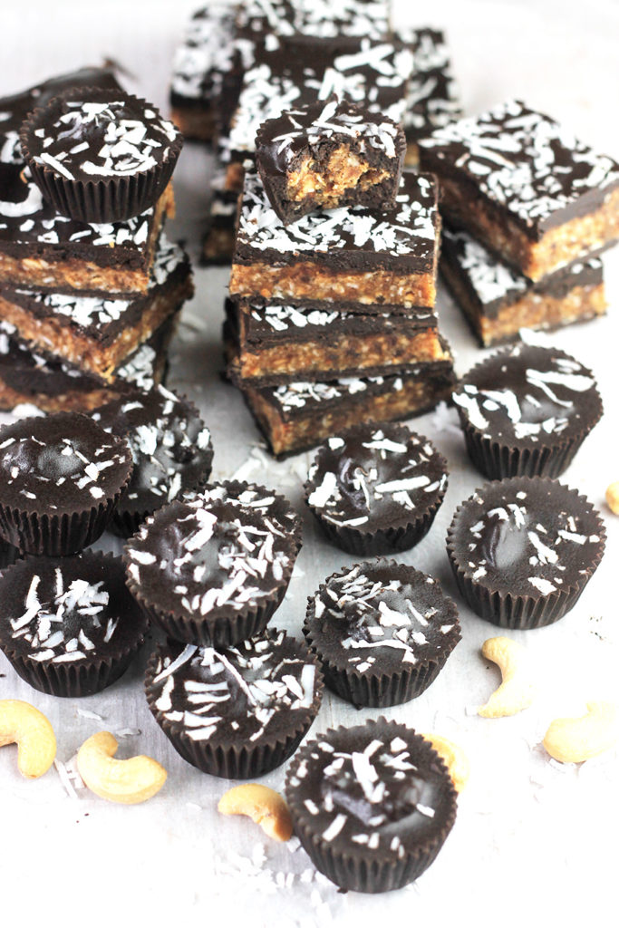 Angled shot of Coconut Cashew Chocolate Cups and a stack of Bars.