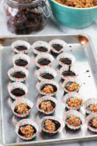 Shallow baking pan filled with mini cupcake liners filled with chocolate and date mixture on top.