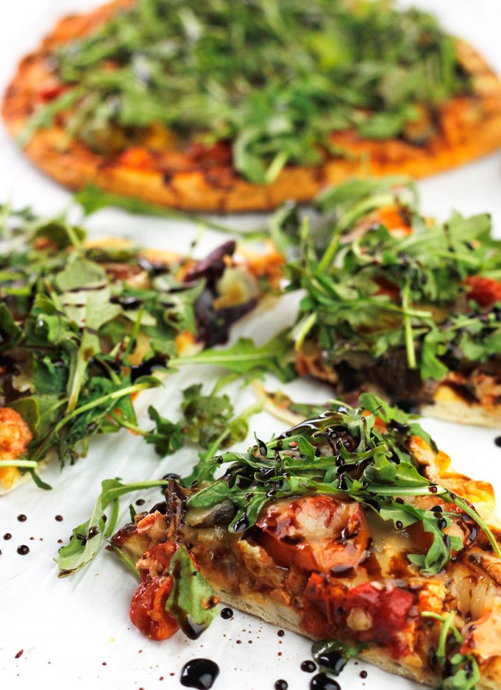 Slices of roasted veggie pizzas topped with arugula greens and drizzled with balsamic glaze.