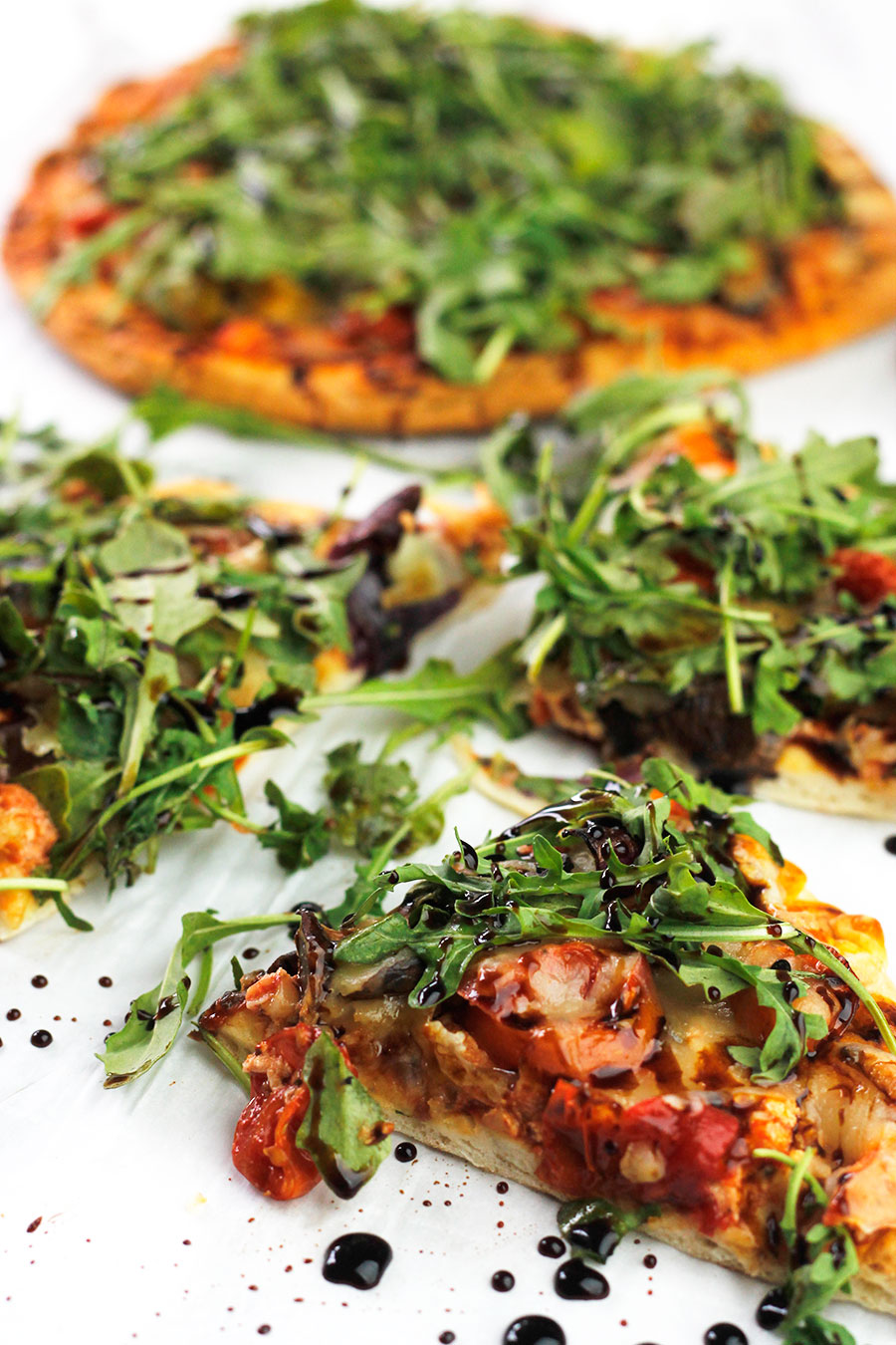 Slices of roasted veggie pizzas topped with arugula greens and drizzled with balsamic glaze.