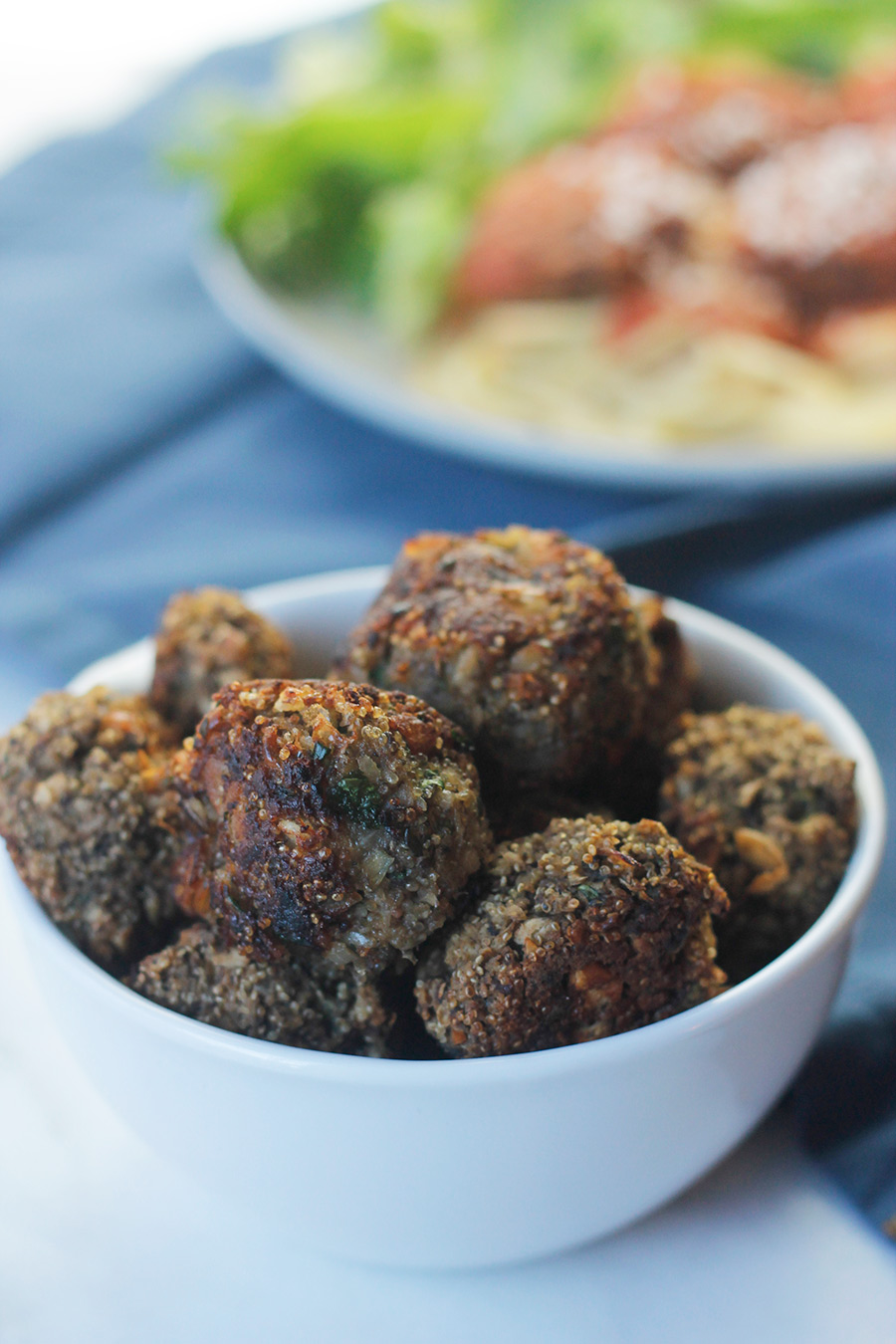 Close-up of bowl of easy meatless meatballs with plate of pasta and salad in background.