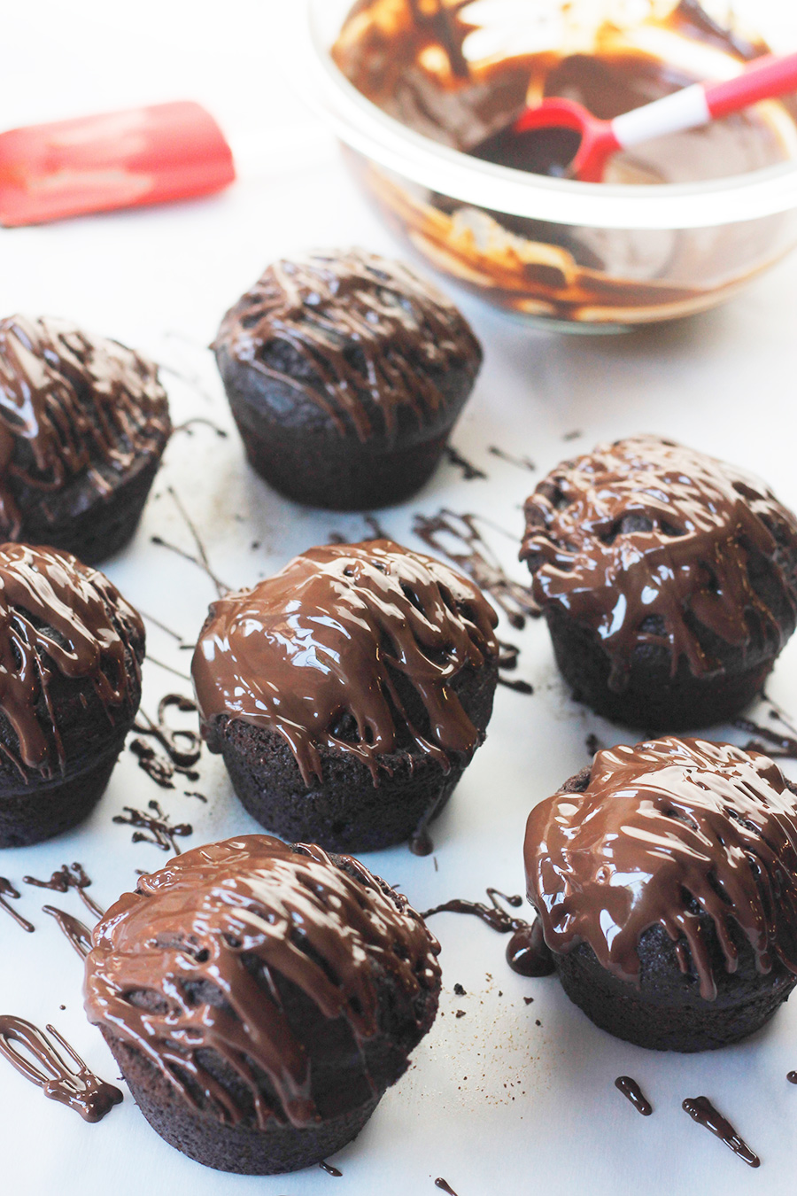 Chocolate-on-chocolate vegan cupcake on white counter with melted chocolate drizzled on top.