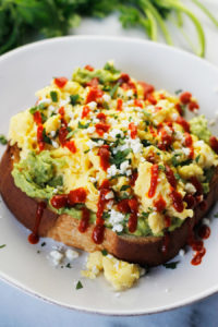 Avocado toast topped with soft scrambled eggs, crumbled queso fresco, fresh torn cilantro and drizzled with sriracha.