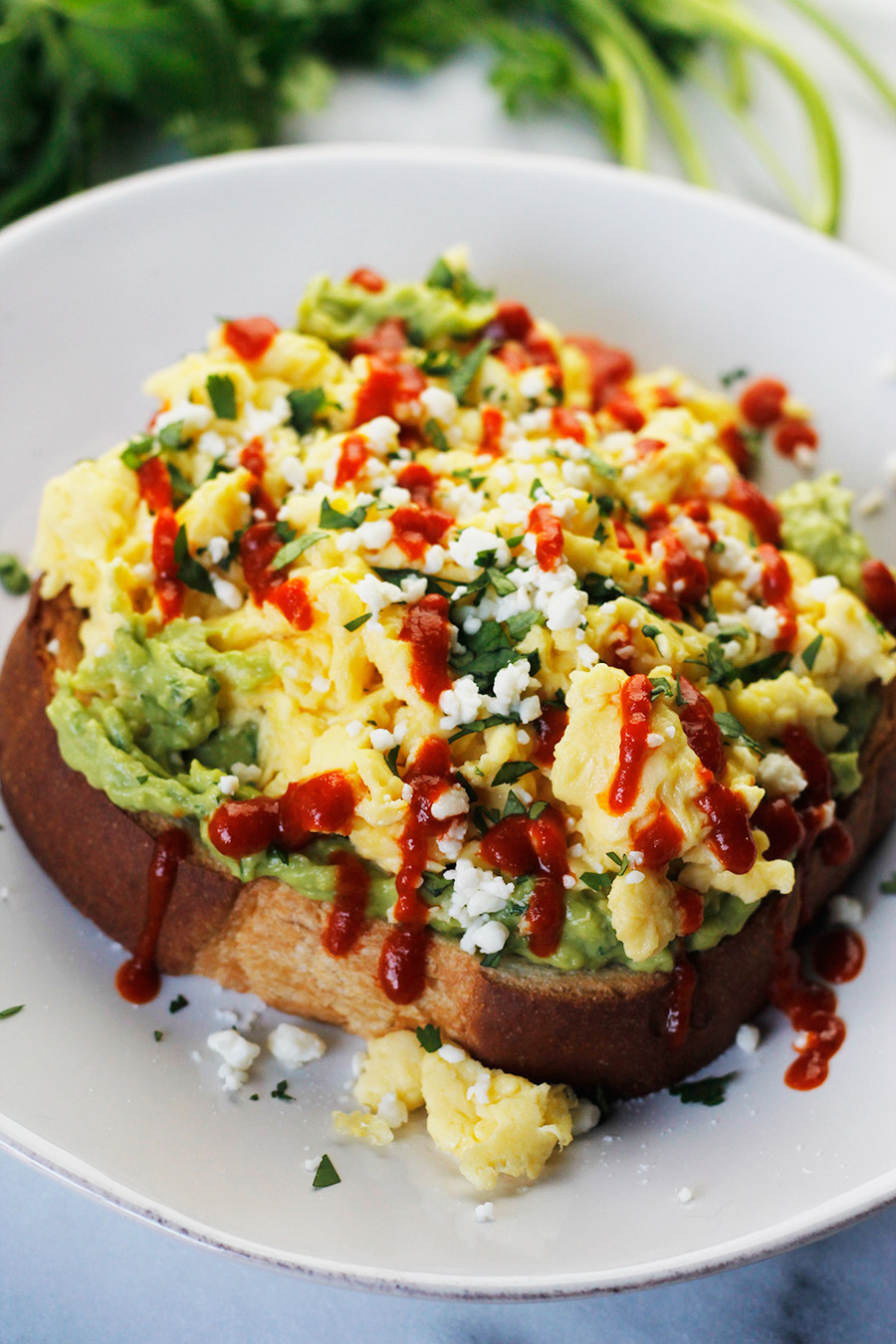 Avocado toast topped with soft scrambled eggs, crumbled queso fresco, fresh torn cilantro and drizzled with sriracha. 
