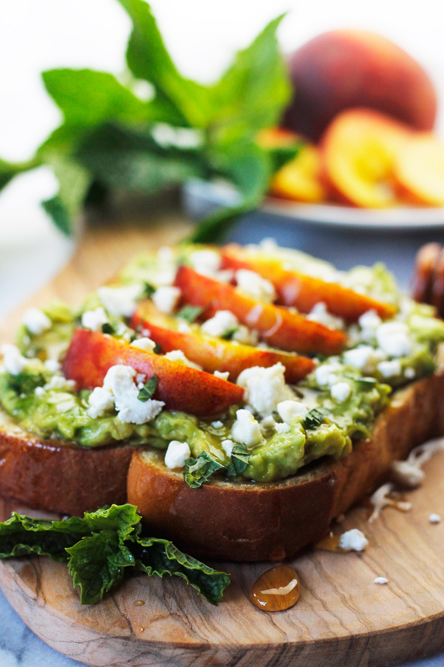 Avocado toast topped with sliced peaches, sprinkled with goat cheese, fresh torn mint leaves and drizzled with honey