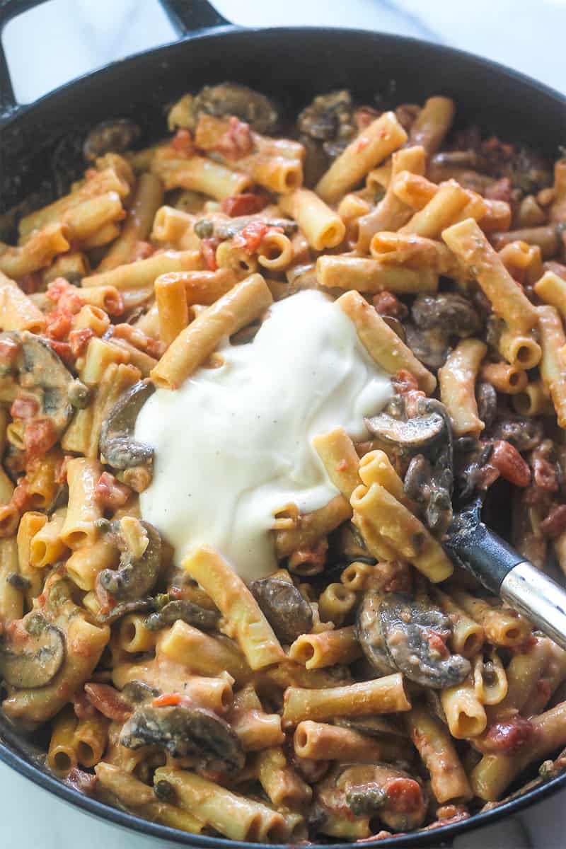 Adding alfredo sauce to cooked one-pot vegetarian pasta.