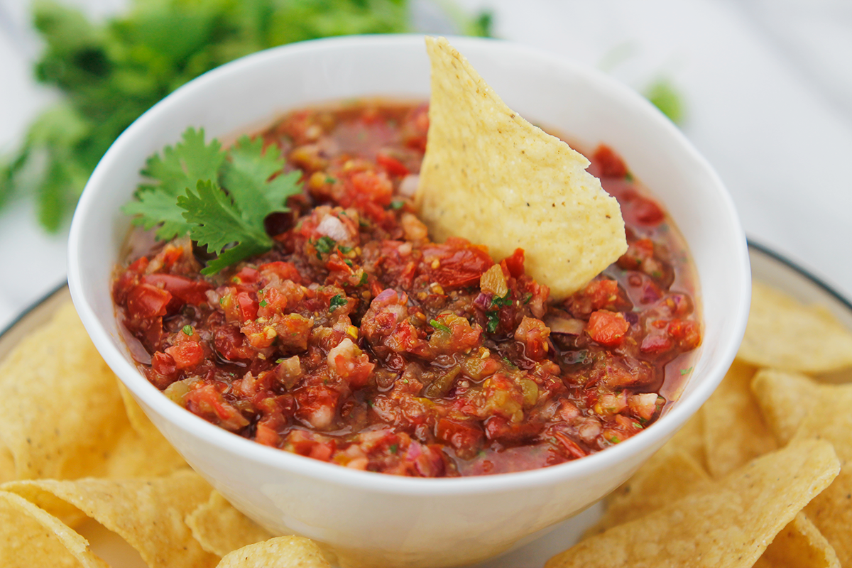 Bowl of salsa on a plate of tortilla chips.