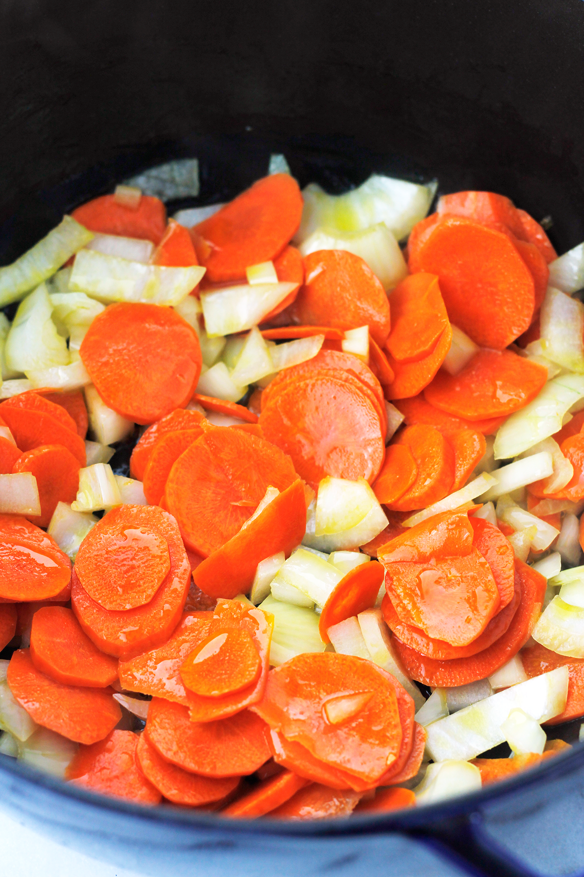 Sliced carrots and onions sauteing in pan.
