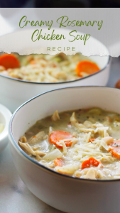 Close-up shot of a bowl of creamy rosemary chicken soup with half of a small bowl of shredded parmesan cheese shown to the left side of the bowl and another bowl of soup in the background.