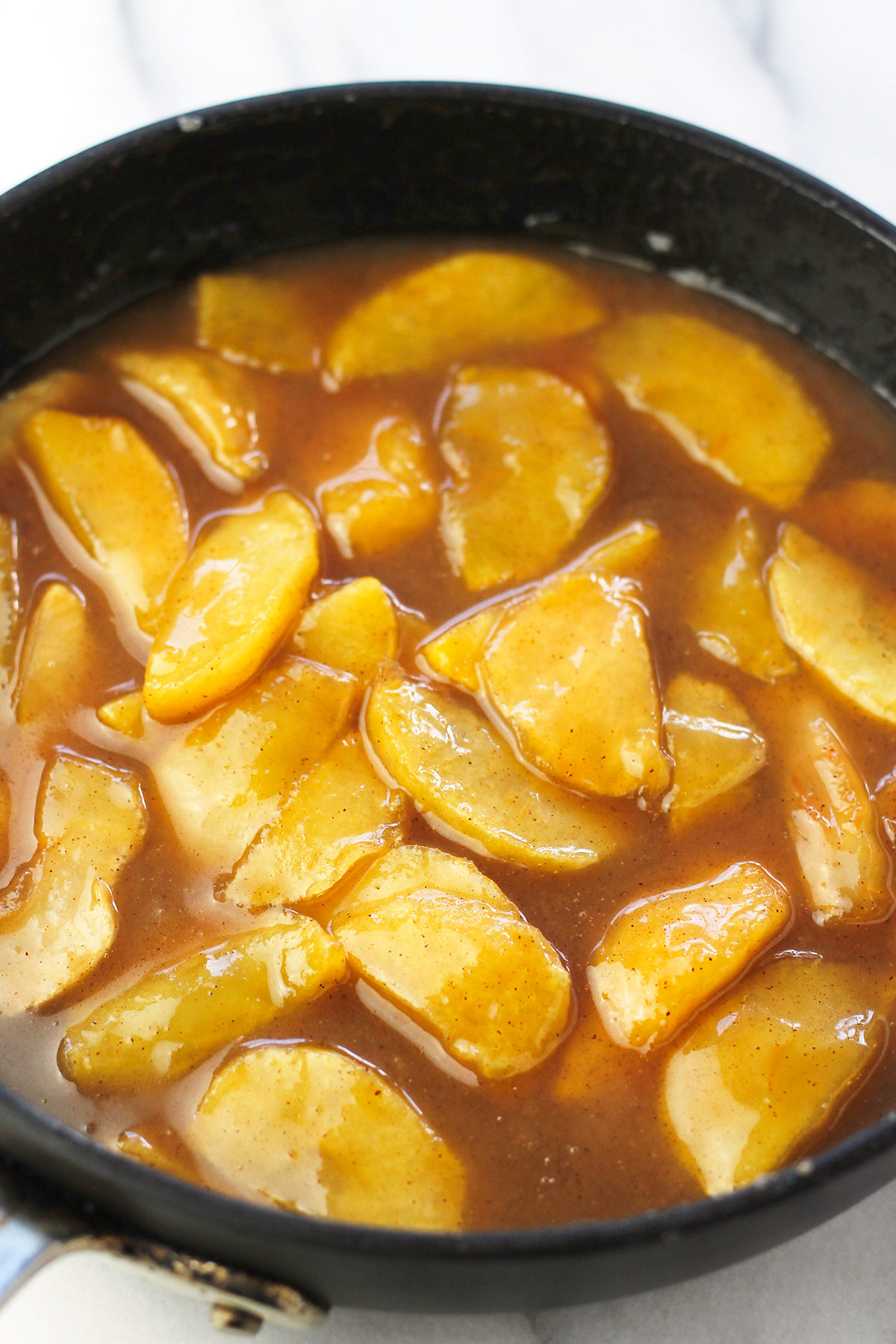 Pan of cooked sliced apples in pumpkin caramel sauce.