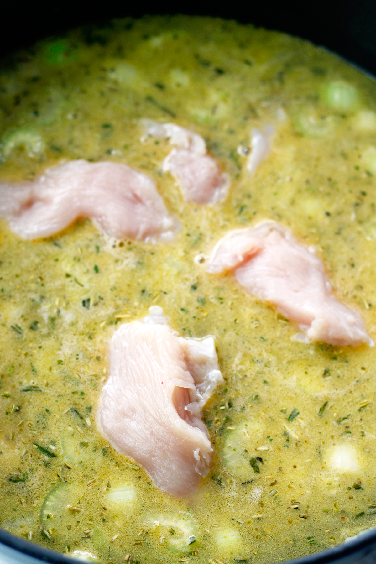 Raw chicken pieces being added to soup.